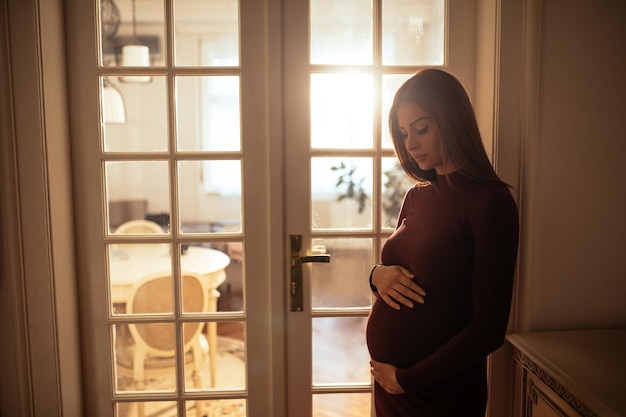 Una bella donna incinta sta facendo il bagno nel sole indiretto nella sua casa accogliente