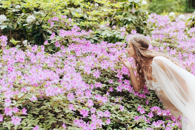 Una bella donna incinta vicino a un cespuglio di rododendro in fiore