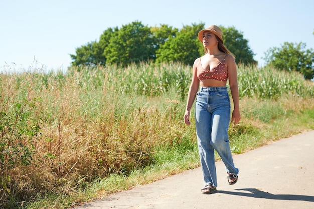 Una bella donna ispanica che indossa un cappello da cowboy che cammina sulla strada in campagna in una giornata di sole