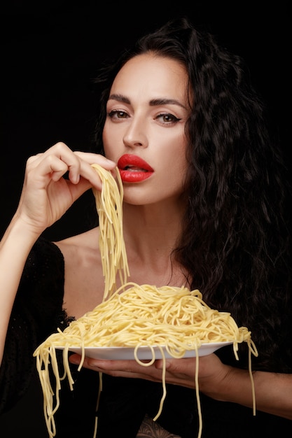 Una bella donna mangia gli spaghetti con le sue mani da un piatto pieno