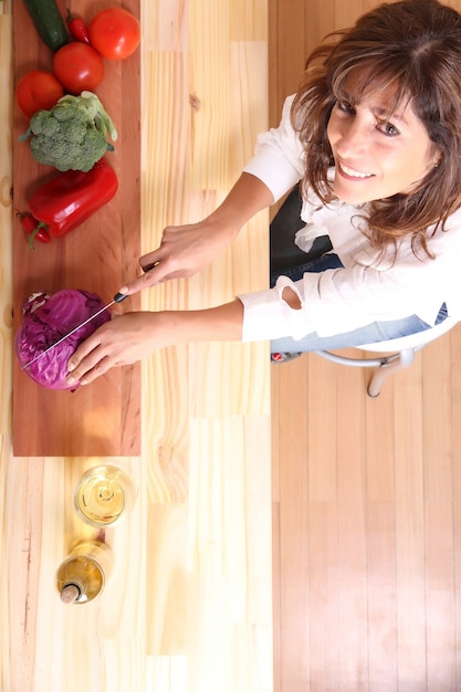 Una bella donna matura che taglia le verdure in cucina.