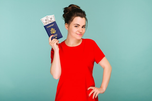 Una bella donna matura in possesso di un passaporto con dollari di denaro su un'immagine di sfondo blu