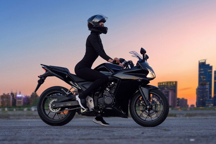 Una bella donna motociclista appoggiata alla sua superbike fuori da un edificio.