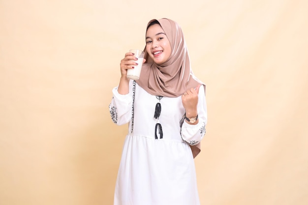 Una bella donna musulmana asiatica che indossa un hijab sorride sì e porta un bicchiere di latte bianco da bere