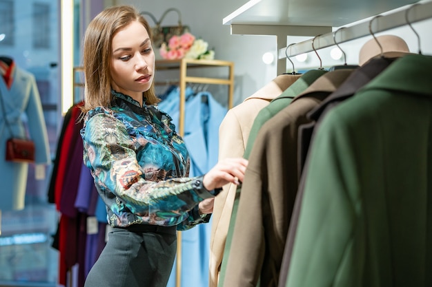 Una bella donna sceglie un cappotto nel negozio