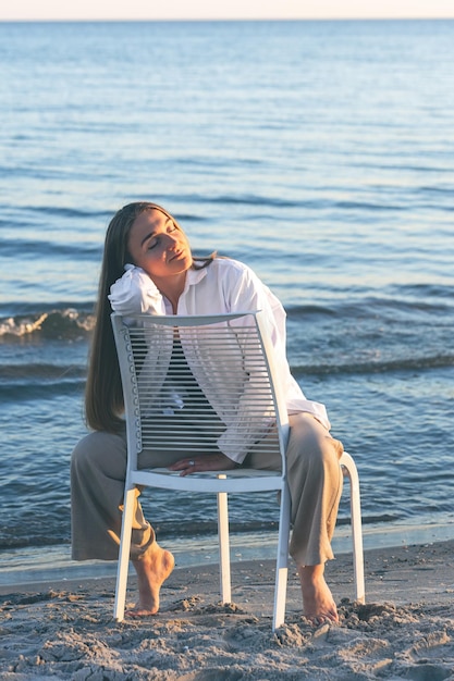 Una bella donna si siede su una sedia vicino al mare