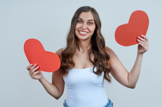 Una bella donna sorridente in una maglietta bianca, con due cuori rossi nelle sue mani