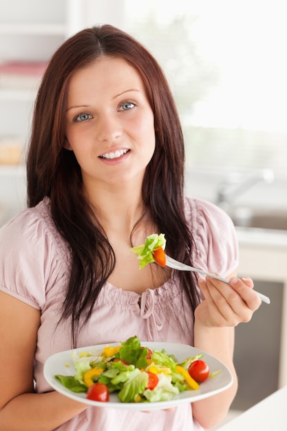 Una bella donna tiene un&#39;insalata mentre guarda nell&#39;obiettivo