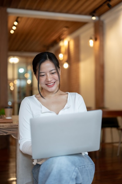 Una bella e felice donna asiatica usa il suo portatile mentre è seduta in un bar