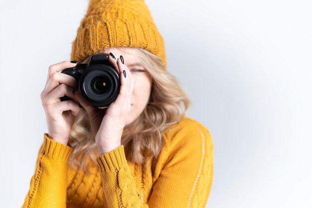 Una bella fotografa con un cappello a maglia viene fotografata con una macchina fotografica in mano in uno studio fotografico