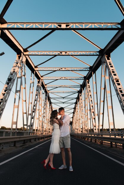 Una bella giovane coppia innamorata, un uomo e una donna, si abbracciano, si baciano su un grande ponte di metallo al tramonto.