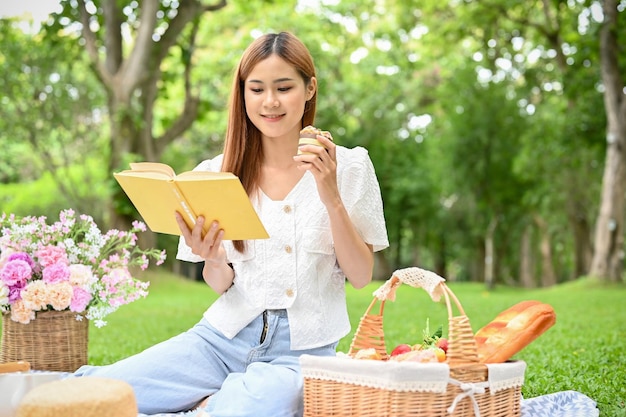 Una bella giovane donna asiatica che fa un picnic nel bellissimo parco cittadino si rilassa mentre legge un libro