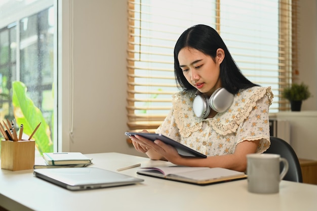 Una bella giovane donna asiatica che usa un tablet digitale e prende appunti, naviga su Internet, lavora da remoto e sta online.