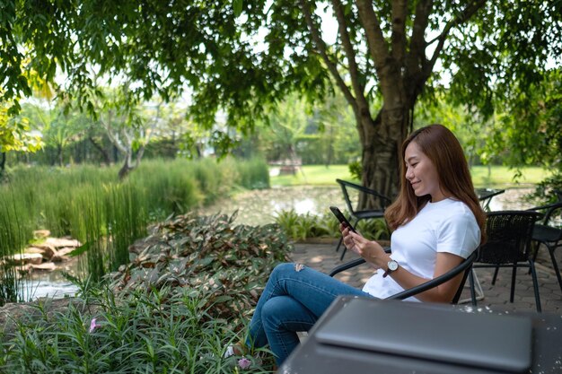 Una bella giovane donna asiatica che utilizza il telefono cellulare con il computer portatile sul tavolo nel parco