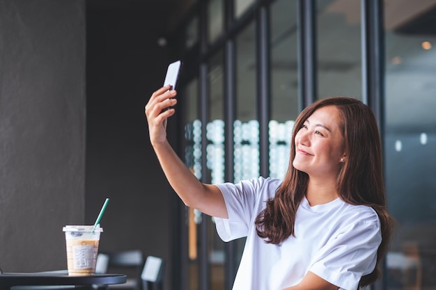 Una bella giovane donna asiatica che utilizza il telefono cellulare per fare un selfie nella caffetteria
