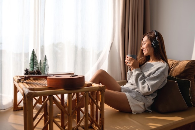 Una bella giovane donna asiatica si diverte a bere caffè e ad ascoltare musica con le cuffie a casa