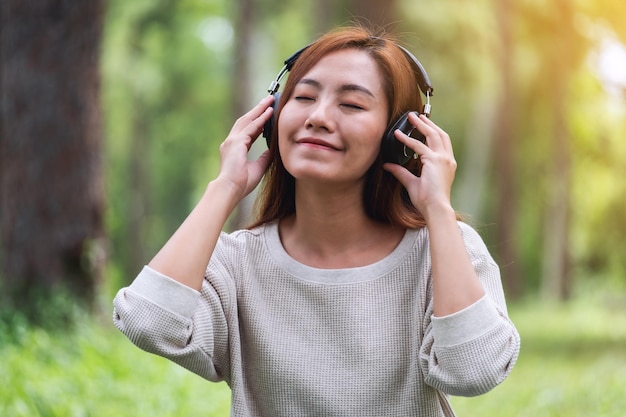 Una bella giovane donna asiatica si diverte ad ascoltare musica con le cuffie sentendosi felice e rilassata nel parco