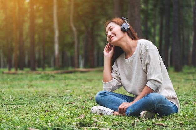 Una bella giovane donna asiatica si diverte ad ascoltare musica con le cuffie sentendosi felice e rilassata nel parco