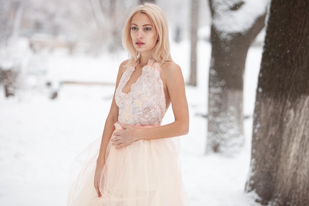 Una bella giovane donna bionda in un abito bianco in posa in un parco invernale innevato. Focalizzazione morbida. Messa a fuoco selettiva