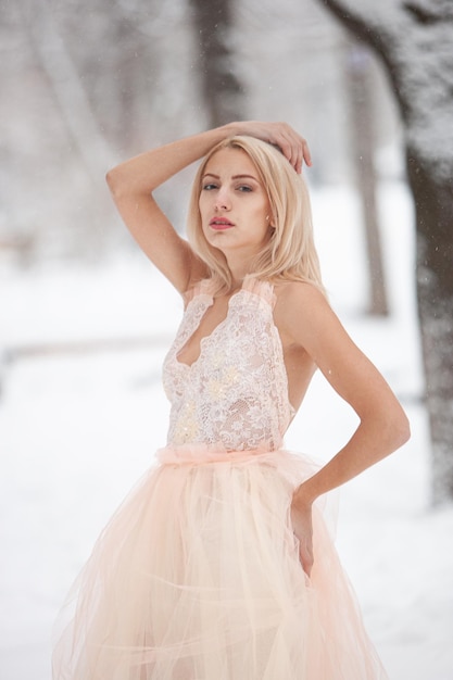 Una bella giovane donna bionda in un abito bianco in posa in un parco invernale innevato. Focalizzazione morbida. Messa a fuoco selettiva