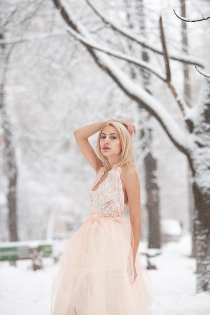 Una bella giovane donna bionda in un abito bianco in posa in un parco invernale innevato. Focalizzazione morbida. Messa a fuoco selettiva