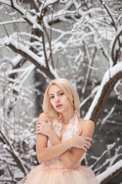 Una bella giovane donna bionda in un abito bianco in posa in un parco invernale innevato. Focalizzazione morbida. Messa a fuoco selettiva