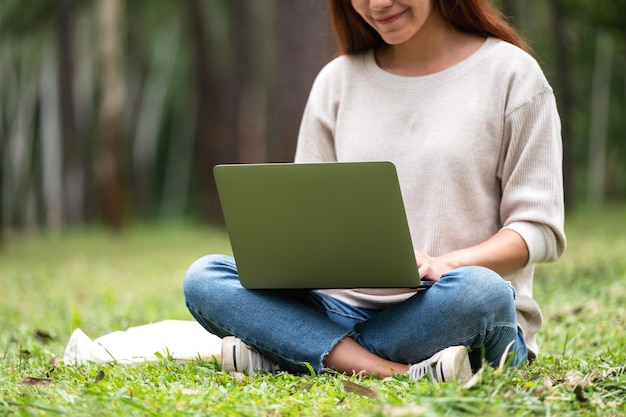 Una bella giovane donna che lavora e digita sulla tastiera del laptop mentre è seduto nel parco