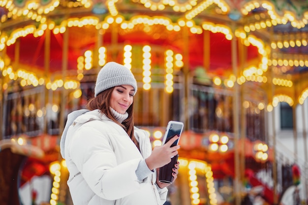 Una bella giovane donna che per mezzo del telefono all'aperto durante le vacanze di Natale