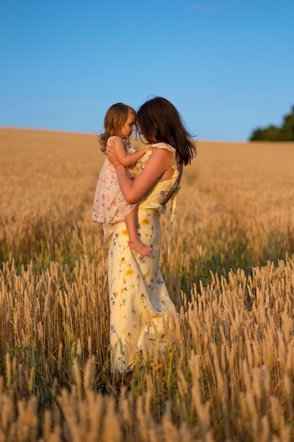 Una bella giovane donna che tiene in braccio la sua bambina in un campo al tramonto Una donna con un bambino in un bellissimo vestito giallo posa al tramonto in un campo