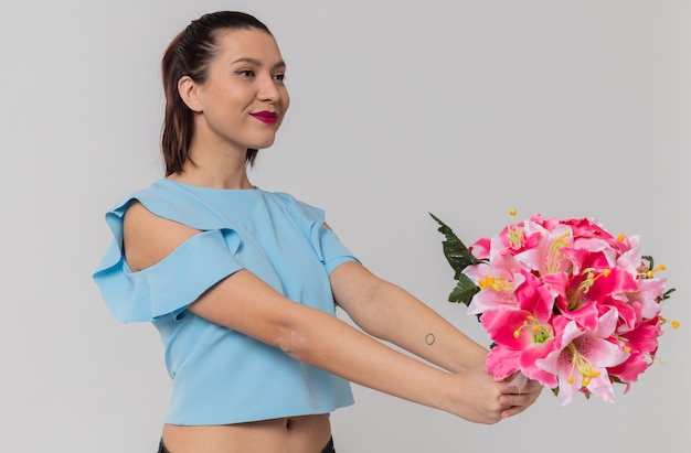 Una bella giovane donna contenta che tiene in mano un mazzo di fiori in piedi di lato