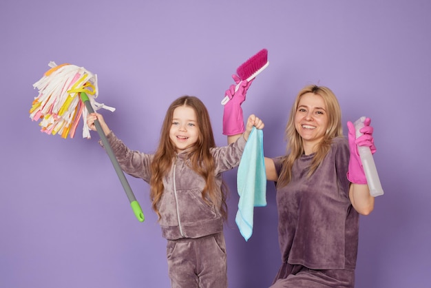 Una bella giovane donna e la sua piccola figlia allegra stanno pulendo la casa stanno tenendo prodotti per la pulizia e sorridendo il concetto di pulizia