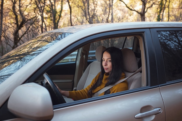 Una bella giovane donna felice alla guida della sua auto nel bosco. l'idea e il concetto di viaggio e scoperta, Fall Getaway