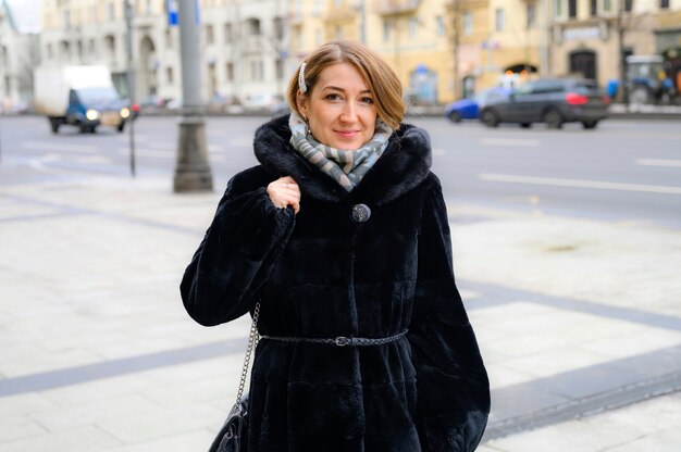 Una bella giovane donna felice in pelliccia invernale alla moda cammina lungo una strada cittadina