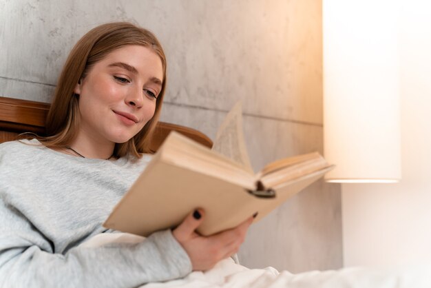 una bella giovane donna felice positiva all'interno a casa nel libro di lettura del letto.