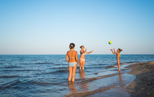 Una bella giovane donna gioca a palla con le sue affascinanti figlie mentre nuota in mare in una calda giornata estiva di sole. Concetto di vacanza con i bambini. Spazio pubblicitario