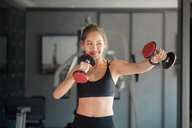 Una bella giovane donna in abiti sportivi che si esercita con i manubri in palestra, il concetto di stile di vita sano, sport, formazione, benessere e sport