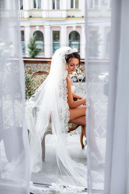 Una bella giovane donna in lingerie squisita si trova sul balcone di un edificio a più piani e tiene in mano un grande mazzo di bellissimi fiori La mattina della sposa il giorno del matrimonio