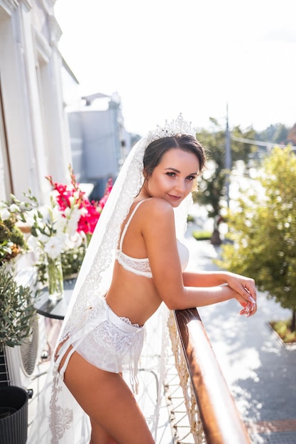 Una bella giovane donna in lingerie squisita si trova sul balcone di un grattacielo Mattina della sposa il giorno del matrimonio