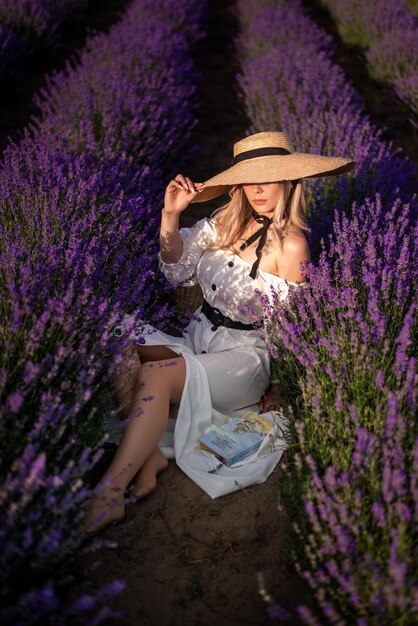 Una bella giovane donna in un vestito bianco è seduta in un campo di lavanda