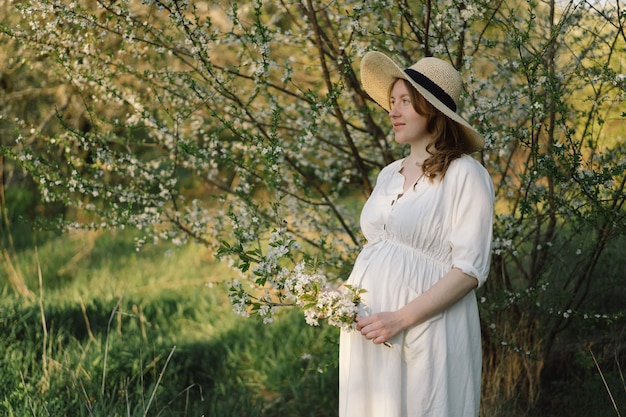 Una bella giovane donna incinta in un abito bianco cammina nel giardino primaverile