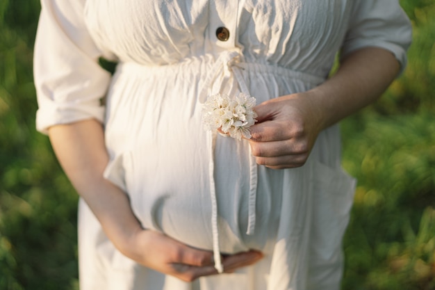 Una bella giovane donna incinta in un abito bianco cammina nel giardino primaverile