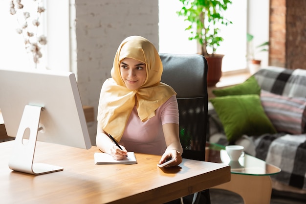 Una bella giovane donna musulmana a casa durante la quarantena e l'autoisolamento. Modello femminile arabo che trascorre del tempo utile per essere isolato. Concetto di assistenza sanitaria, comunicazione, educazione durante la pandemia.