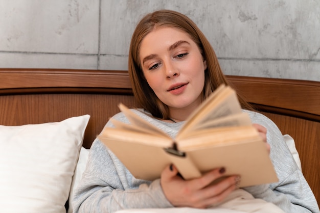 una bella giovane donna seria concentrata all'interno a casa nel libro di lettura del letto.