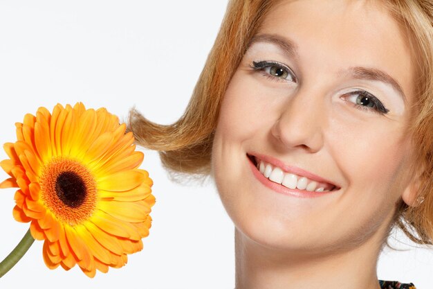 Una bella giovane donna sorridente in un abito bianco con un fiore rosso brillante vicino al viso