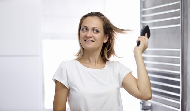 Una bella giovane donna sta guardando il suo riflesso in bagno e si pettina i capelli