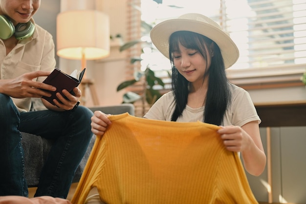 Una bella giovane donna sta impacchettando i vestiti nella valigia e si sta preparando per il viaggio di vacanza.