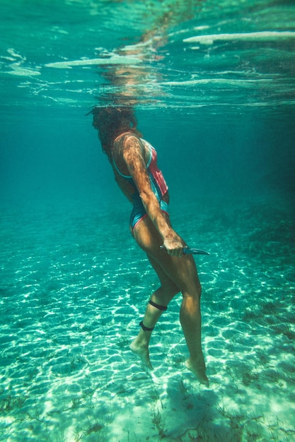 Una bella giovane donna sta nuotando sott'acqua godendosi il blu del mare.