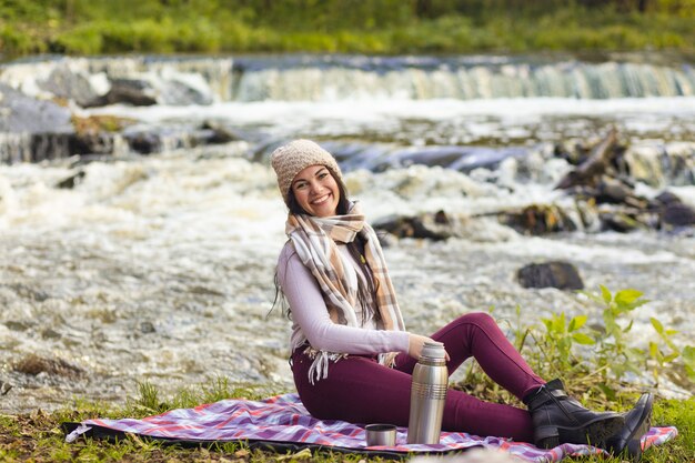 Una bella giovane donna sta riposando sulle rive di un fiume autunnale