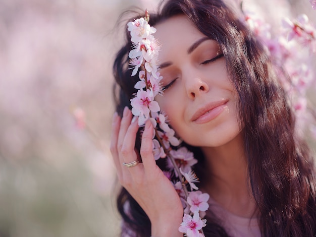 Una bella giovane donna vicino a un albero in fiore di ciliegio primaverile in fiore. Un ritratto di luce incredibilmente gentile