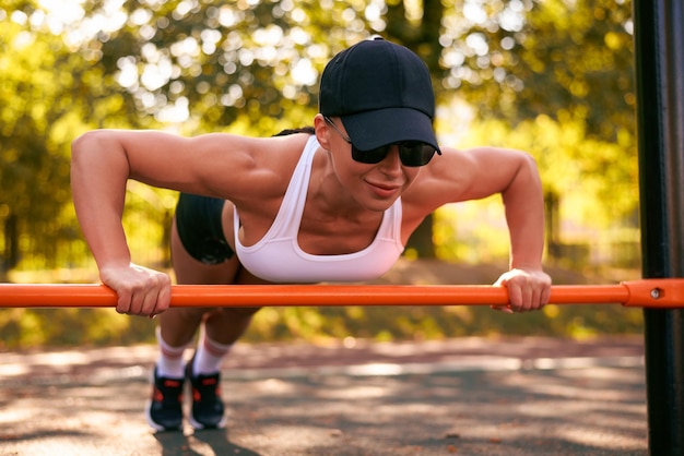 Una bella giovane fitness girl si sta scaldando allo stadio prima dell'allenamento Una brunetta attraente e snella con un cappello nero e occhiali da sole Stile di vita attivo